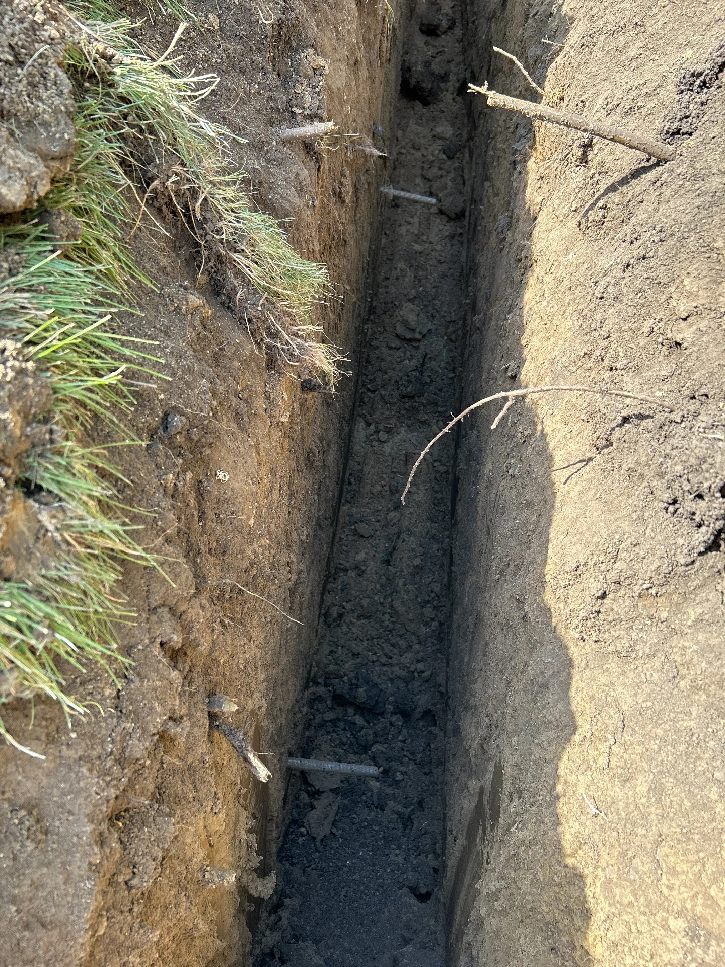 Open drainage trench beside a Kansas City metro home exposing dense clay soil